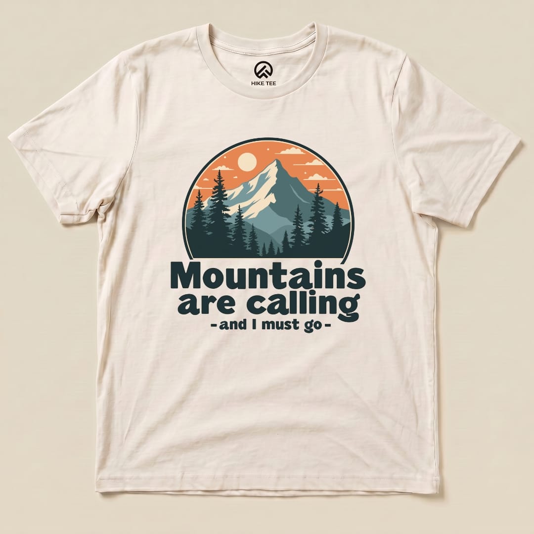 A light-colored graphic t-shirt featuring a mountain scene with the phrase "Mountains are calling - and I must go.