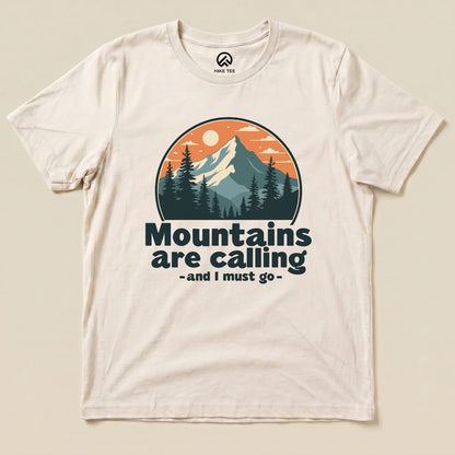 A light-colored graphic t-shirt featuring a mountain scene with the phrase "Mountains are calling - and I must go.