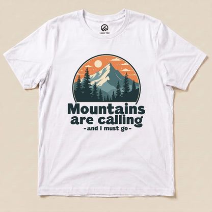 A white graphic t-shirt featuring an illustration of mountains and trees with the text "Mountains are calling - and I must go.