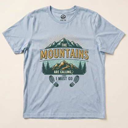 A light blue graphic t-shirt features a design with mountains, trees, and the slogan "The Mountains Are Calling and I Must Go.