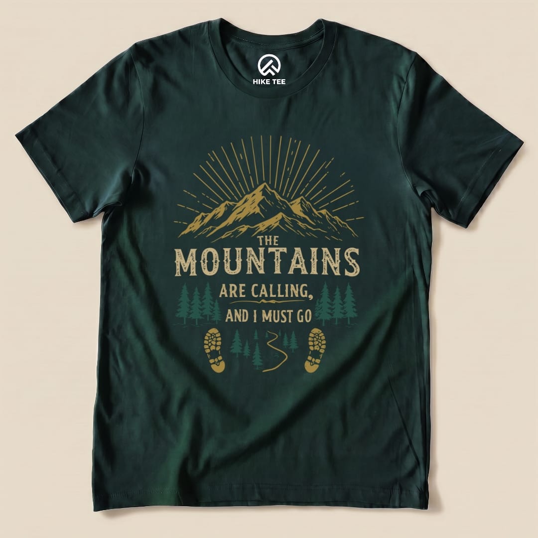A graphic t-shirt featuring the slogan "THE MOUNTAINS ARE CALLING, AND I MUST GO" with mountains, trees, and footprints.