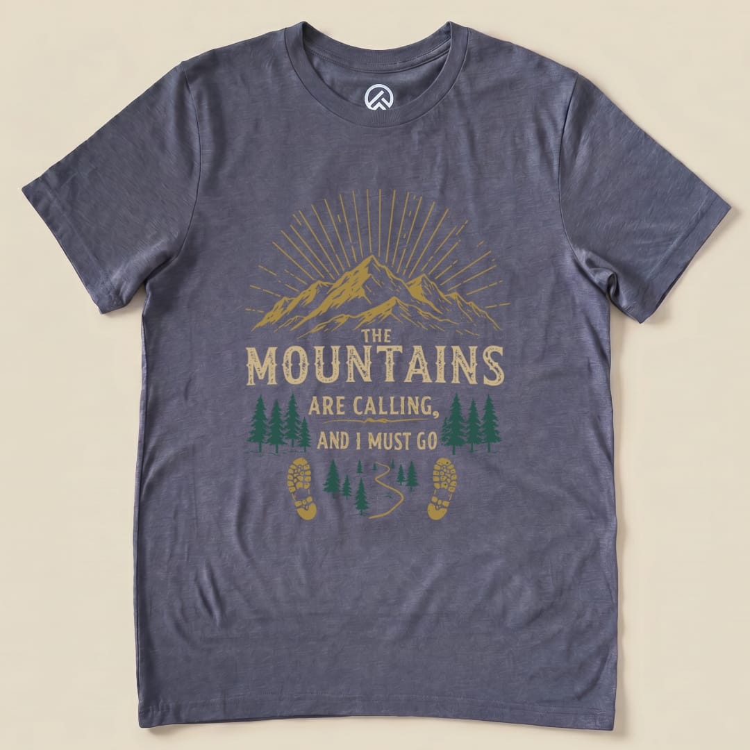 A graphic t-shirt featuring the phrase "THE MOUNTAINS ARE CALLING, AND I MUST GO" above a scenic mountain and forest design.