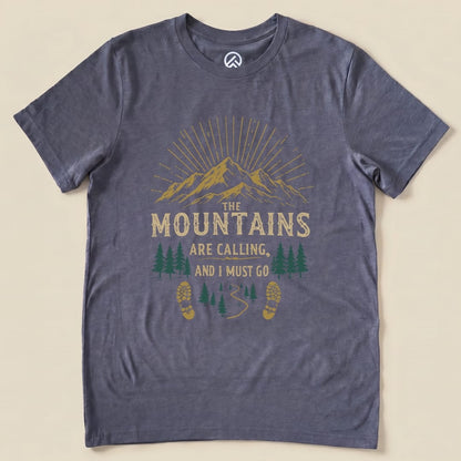 A graphic t-shirt featuring the phrase "THE MOUNTAINS ARE CALLING, AND I MUST GO" above a scenic mountain and forest design.