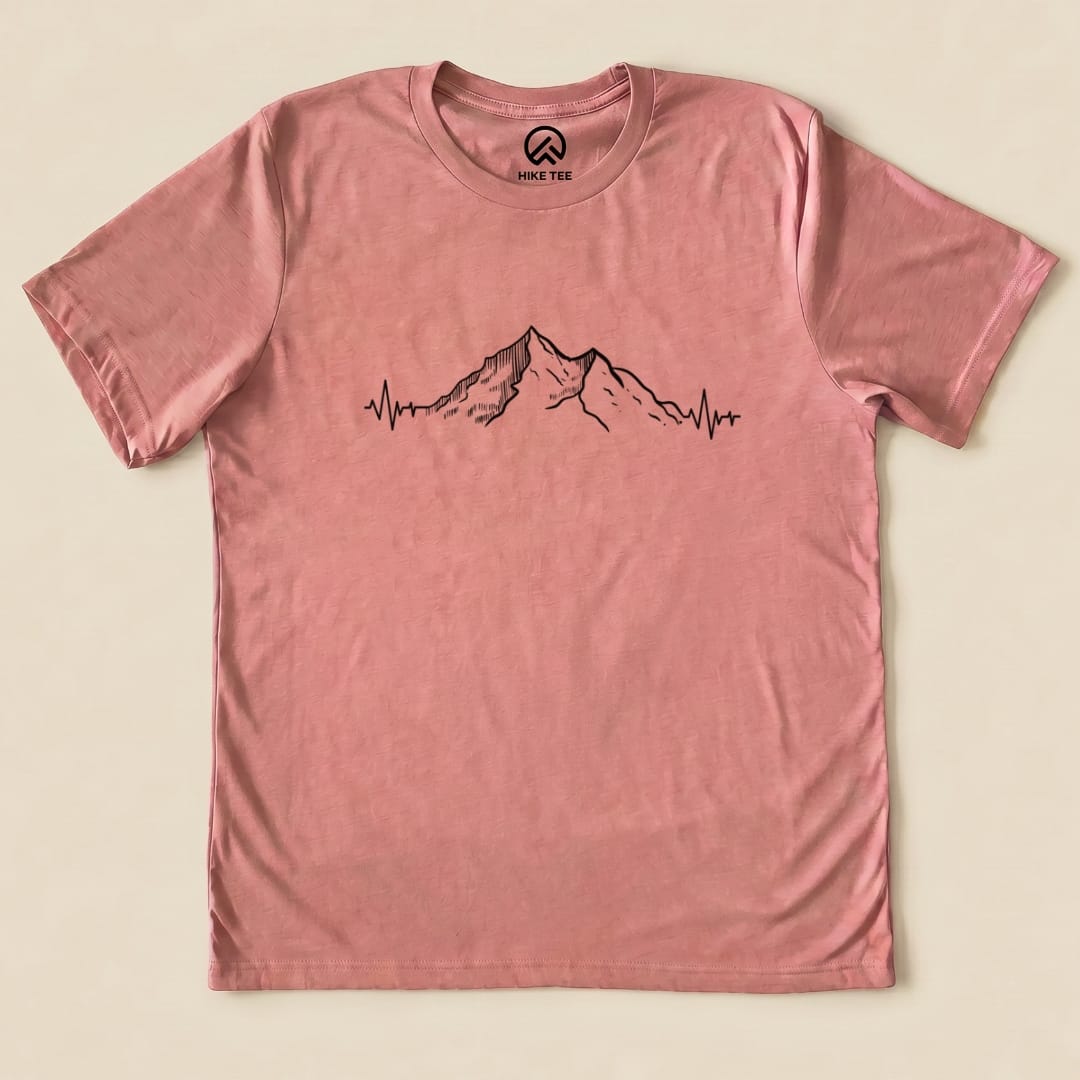 A flat graphic t-shirt in a pink hue featuring a mountain design with heart rate lines, labeled as "Mountains Heart Rate Shirt.