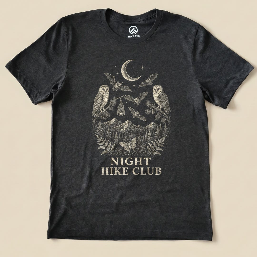 A dark graphic t-shirt featuring an intricate design of owls, bats, mountains, and the text "NIGHT HIKE CLUB".