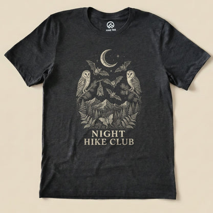 A dark graphic t-shirt featuring an intricate design of owls, bats, mountains, and the text "NIGHT HIKE CLUB".
