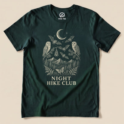 A flat graphic t-shirt in dark green featuring an intricate design of owls, bats, and mountains with the words "NIGHT HIKE CLUB.