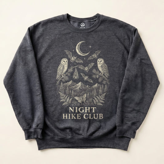 A flat view of a dark sweatshirt featuring an intricate graphic design of two owls, bats, and a mountain scene with "NIGHT HIKE CLUB" text integrated below.