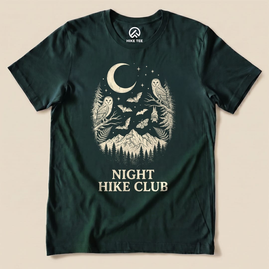 The Night Hike Club Shirt features an intricate graphic of owls, bats, and mountains surrounded by a crescent moon.