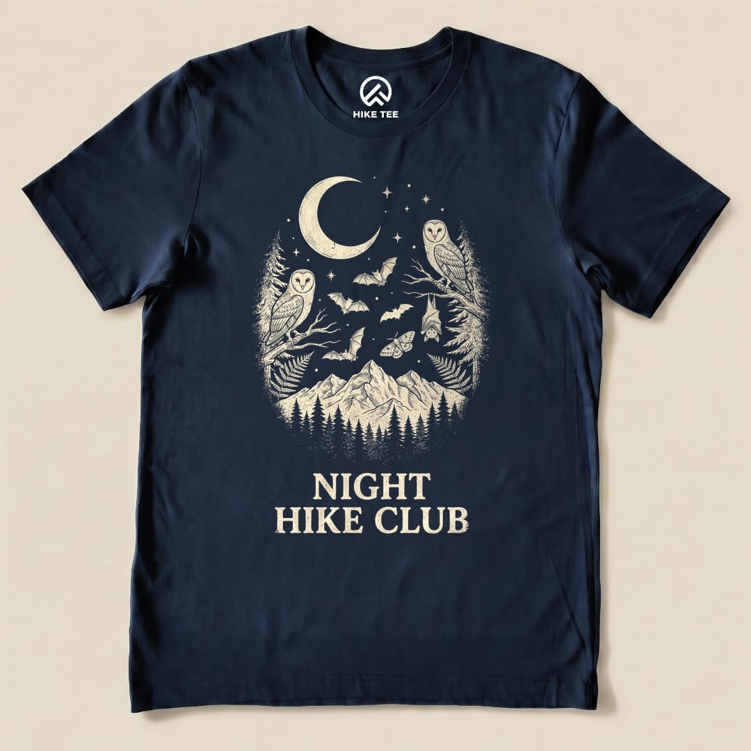 A navy graphic t-shirt featuring the "Night Hike Club Shirt" design with owls, bats, and a mountain scene under a crescent moon.