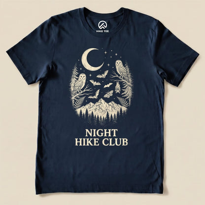 A navy graphic t-shirt featuring the "Night Hike Club Shirt" design with owls, bats, and a mountain scene under a crescent moon.
