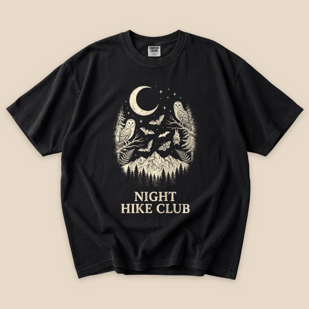 Black graphic t-shirt featuring a moonlit design with owls, bats, and mountains, labeled "Night Hike Club" at the bottom.