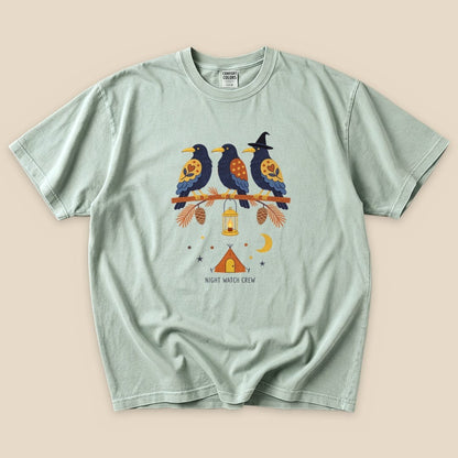 The Night Watch Crew T-Shirt features a graphic of three birds on a branch with a lantern and a tent, set against a whimsical night sky.