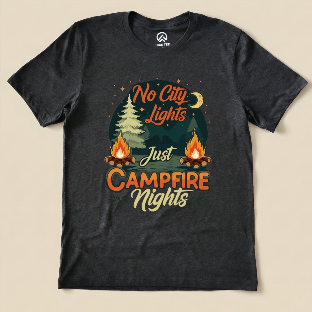 A graphic t-shirt featuring the phrase "No City Lights Just Campfire Nights" with trees and campfires illustrated on a dark background.