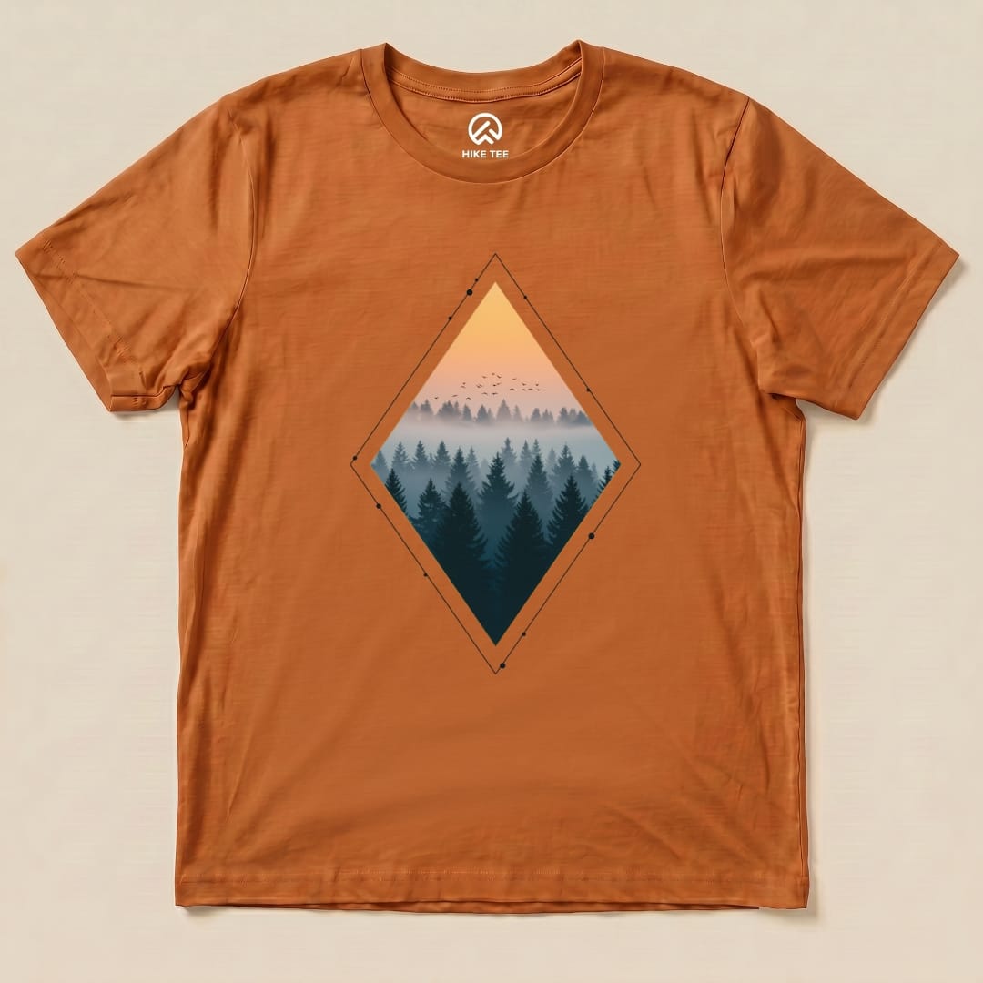 A graphic t-shirt in burnt orange featuring a diamond-shaped print of a foggy forest and sunset, labeled as the "Nostalgic Forest Shirt.