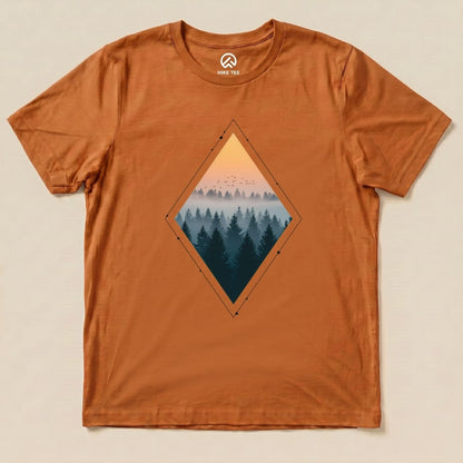 A graphic t-shirt in burnt orange featuring a diamond-shaped print of a foggy forest and sunset, labeled as the "Nostalgic Forest Shirt.