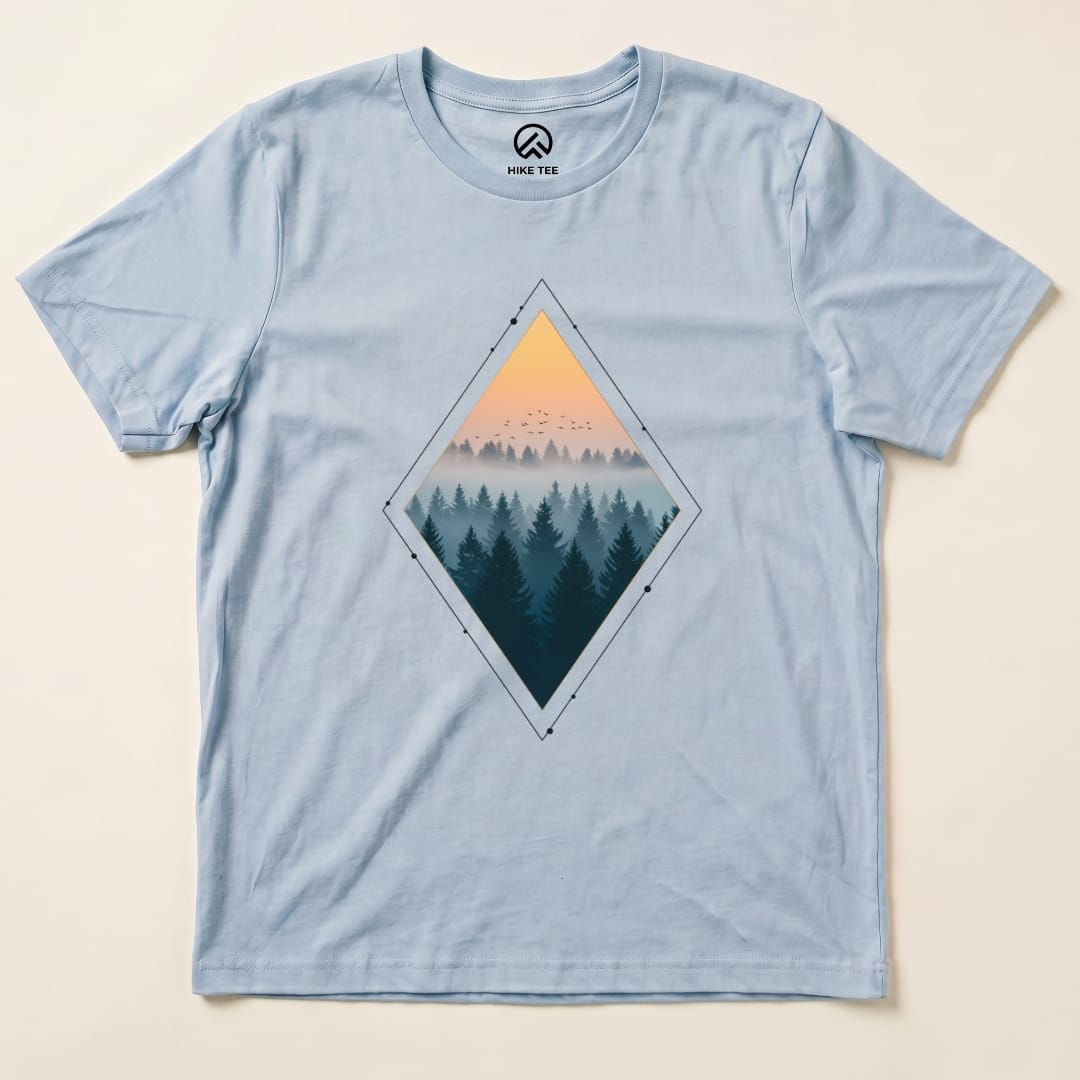 A light blue graphic t-shirt features a diamond-shaped design with a nostalgic forest scene at sunset and birds in the sky, titled "Nostalgic Forest Shirt".