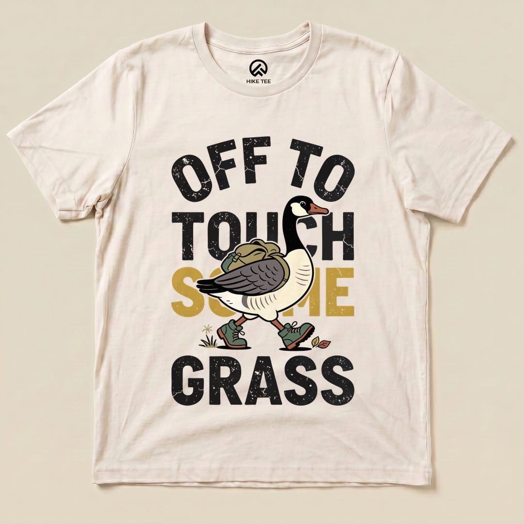 A cream graphic t-shirt featuring a cartoon goose and the phrase "OFF TO TOUCH SOME GRASS" in bold lettering.