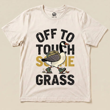 A cream graphic t-shirt featuring a cartoon goose and the phrase "OFF TO TOUCH SOME GRASS" in bold lettering.