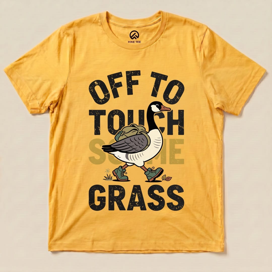 A yellow graphic t-shirt featuring a cartoon goose carrying a backpack with the phrase "Off To Touch Some Grass" prominently displayed.
