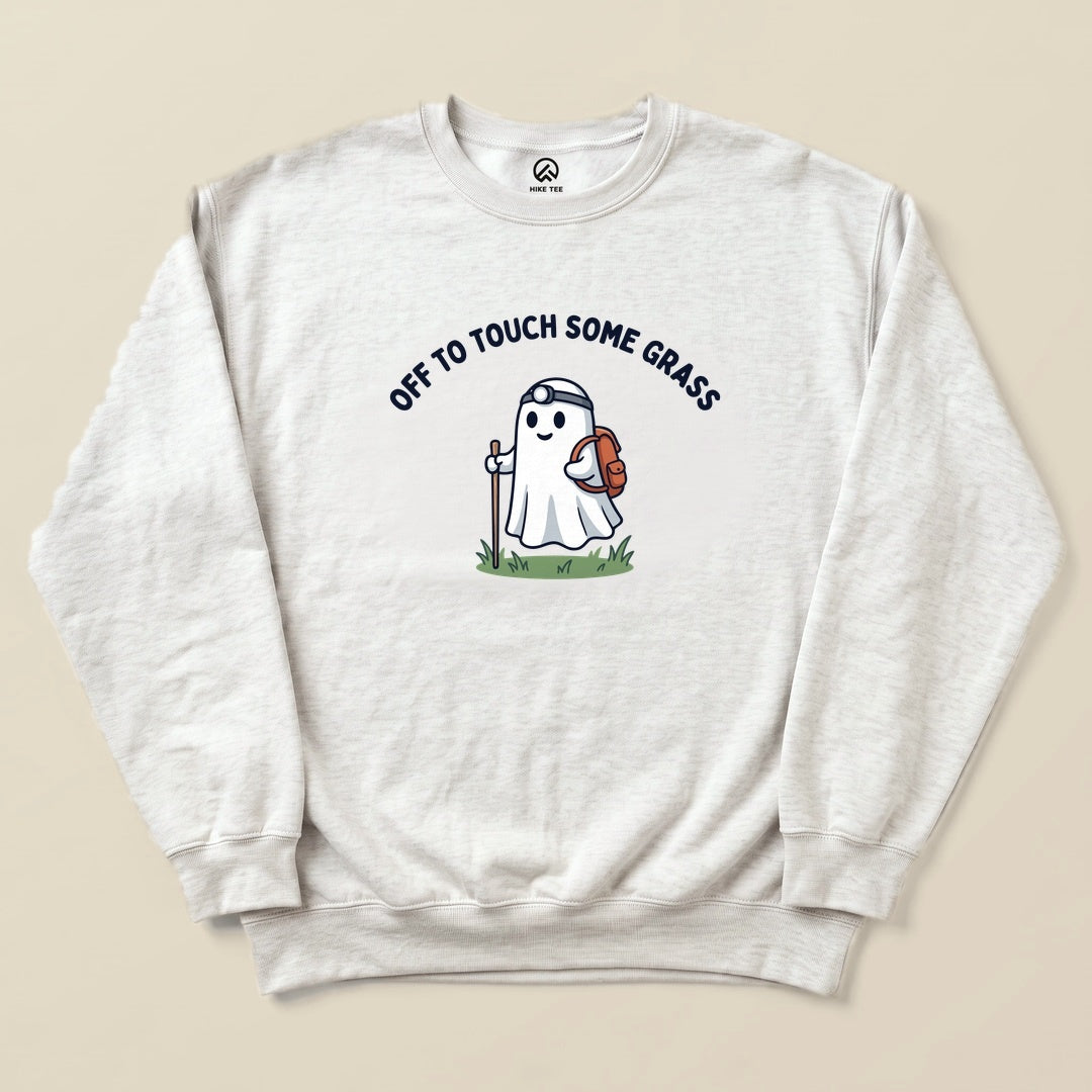 A light gray sweatshirt features a playful ghost character holding a backpack and a walking stick, with the words “OFF TO TOUCH SOME GRASS” above.
