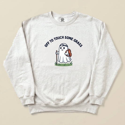A light gray sweatshirt features a playful ghost character holding a backpack and a walking stick, with the words “OFF TO TOUCH SOME GRASS” above.