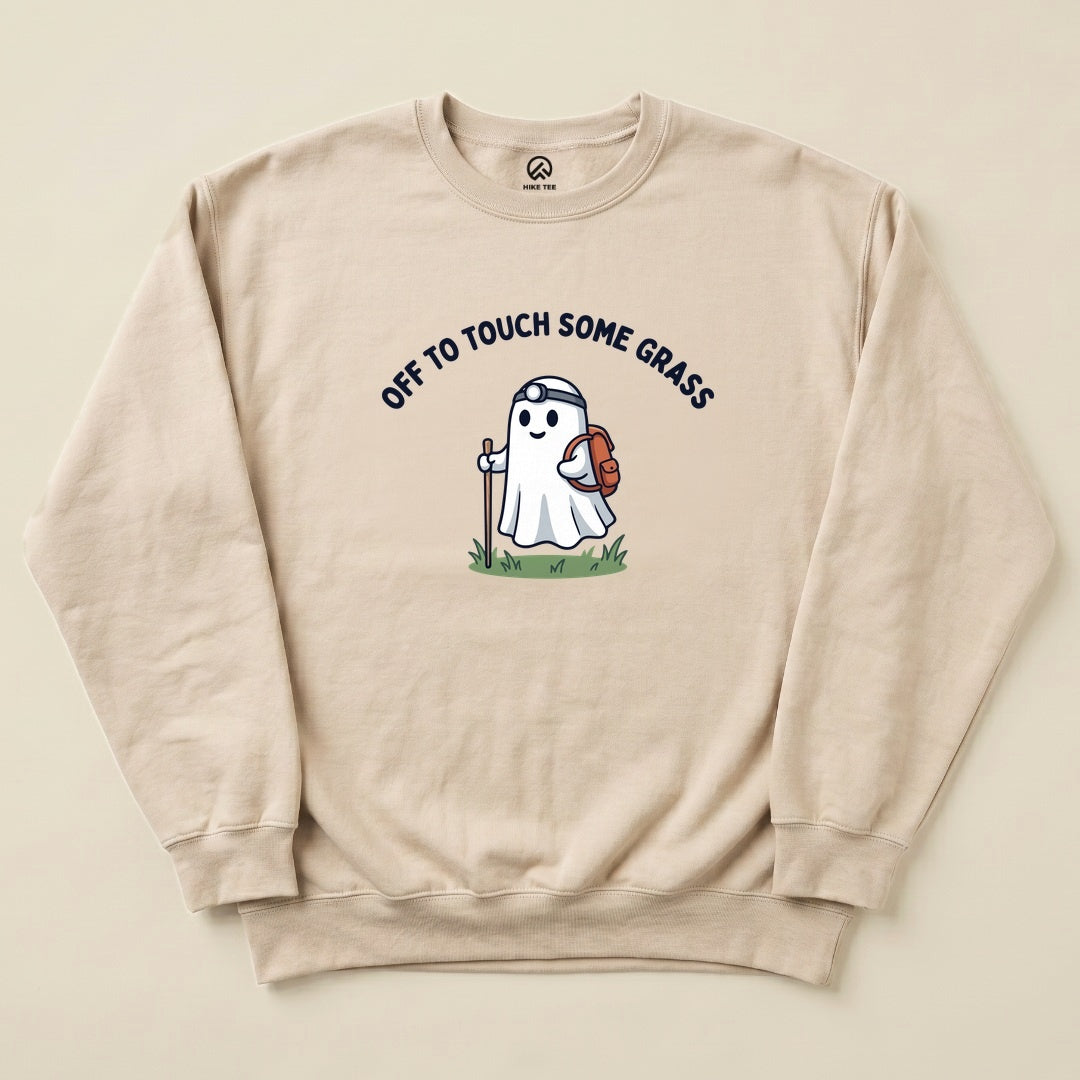 A beige sweatshirt featuring a cartoon ghost with a backpack and hiking stick, printed with "OFF TO TOUCH SOME GRASS".