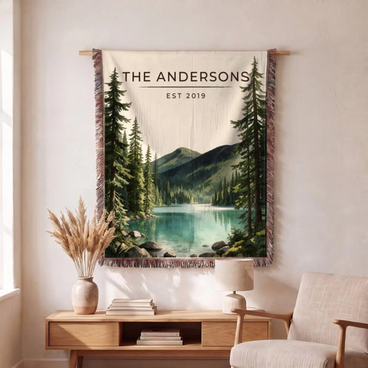 A cozy Olympic Lake Crescent Woven Blanket with lush forest and mountain graphics, displayed elegantly in a modern living room.