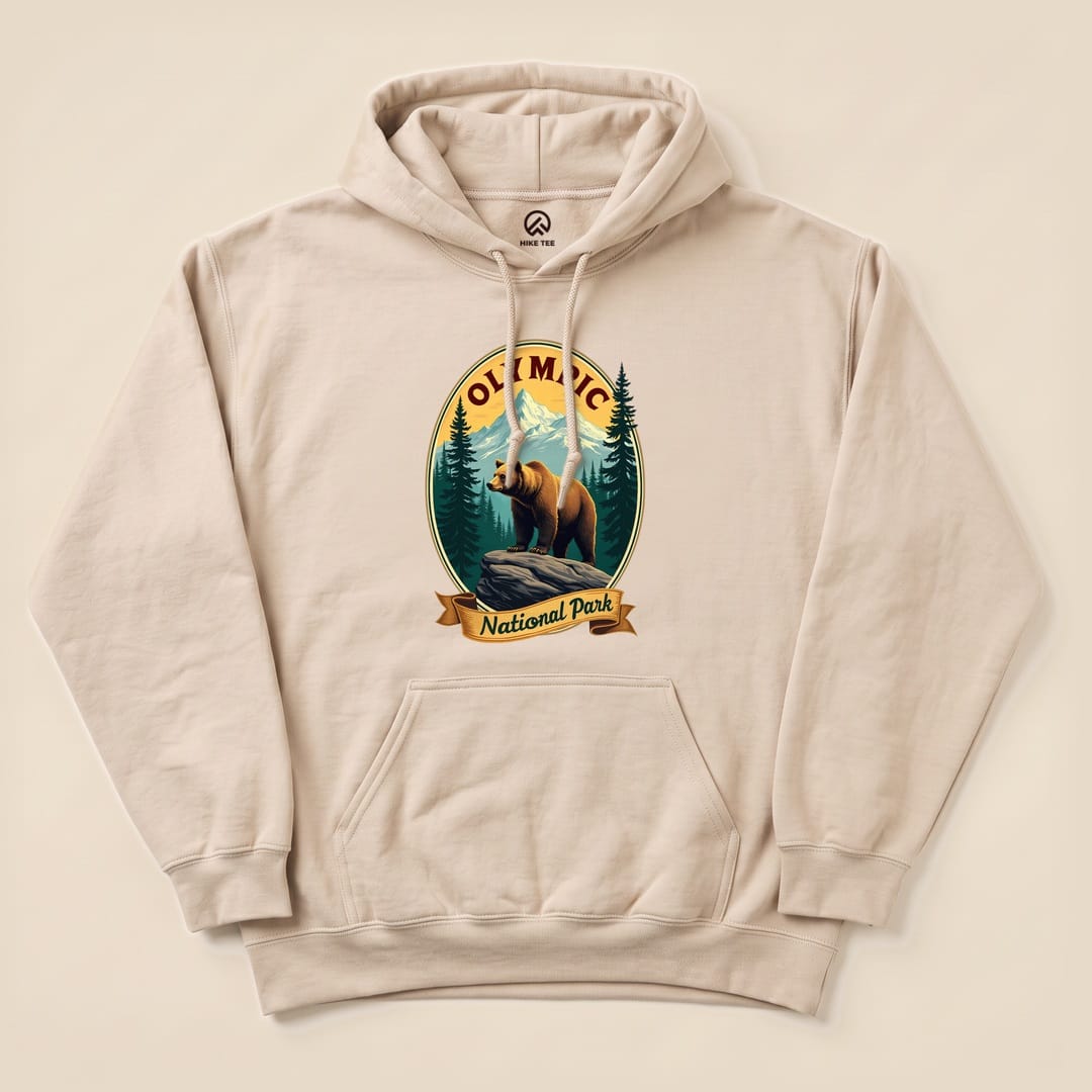 A beige hoodie featuring a graphic of a bear on a rock, with "Olympic National Park" text and surrounding forest details.