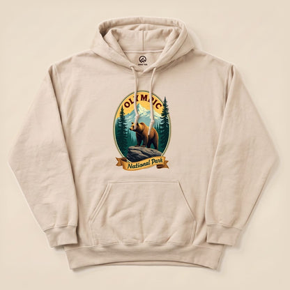 A beige hoodie featuring a graphic of a bear on a rock, with "Olympic National Park" text and surrounding forest details.