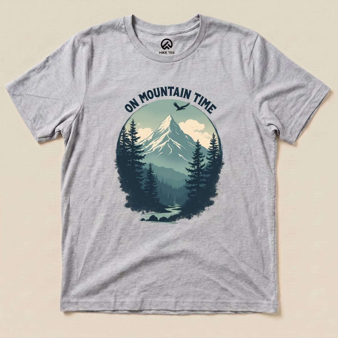 A gray graphic t-shirt featuring the phrase "ON MOUNTAIN TIME" above a serene mountain and forest scene design.