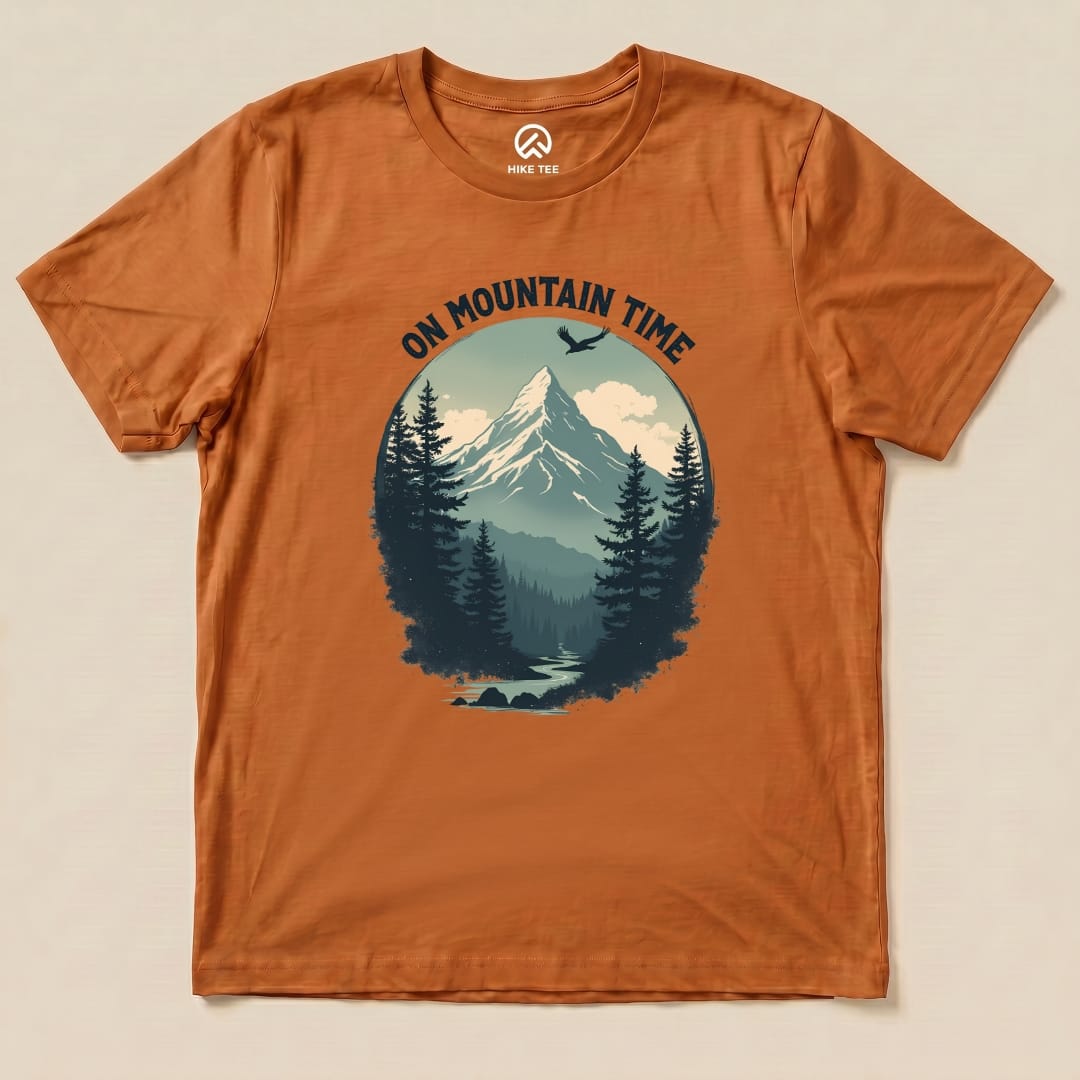 The On Mountain Time Shirt features a scenic mountain graphic surrounded by trees, printed on an orange graphic t-shirt.