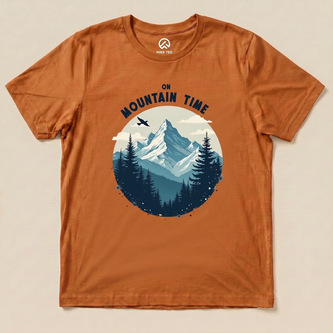 A graphic t-shirt featuring mountains, pine trees, and the text "On Mountain Time" in bold lettering on an orange background.