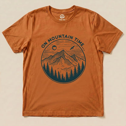 A graphic t-shirt in burnt orange features the phrase "ON MOUNTAIN TIME" above a detailed mountain and forest scene.