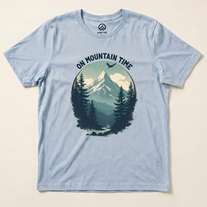 A light blue graphic t-shirt featuring the phrase "ON MOUNTAIN TIME" above a scenic design of mountains and trees.