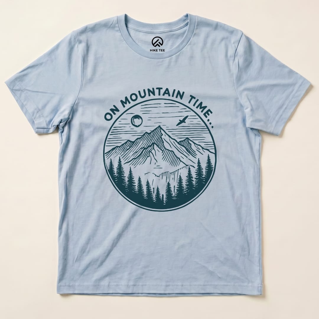The graphic t-shirt features the phrase "ON MOUNTAIN TIME" above a detailed illustration of mountains, pine trees, and a sun.