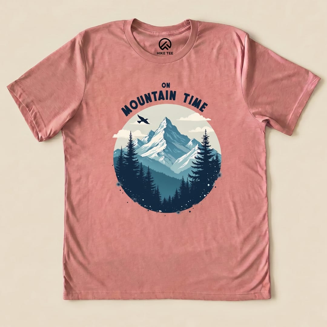 A graphic t-shirt in a light pink hue features a mountain landscape with the words "On Mountain Time" above, surrounded by trees.