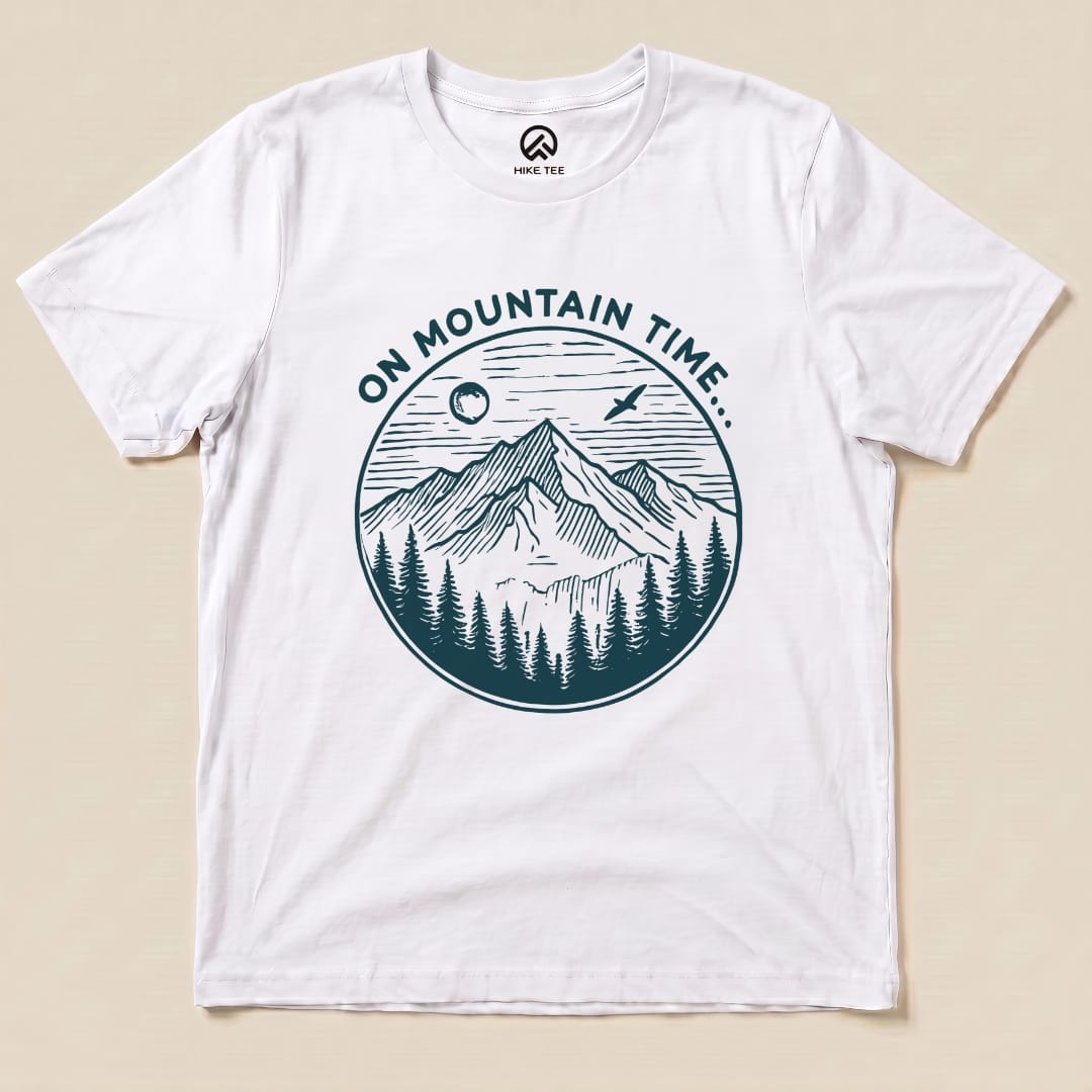A white graphic t-shirt featuring a design with mountains, trees, and the phrase "ON MOUNTAIN TIME..." in an illustrated circle.