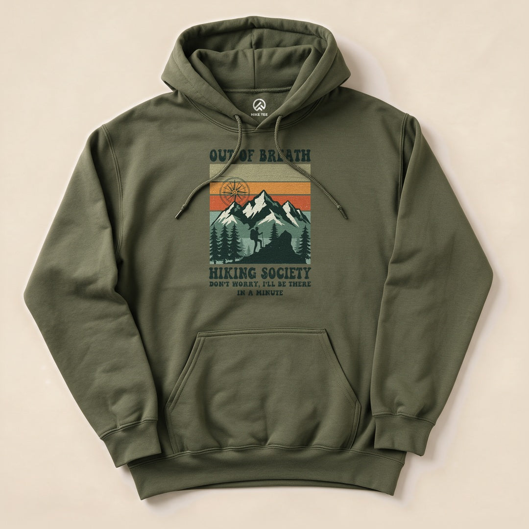A graphic hoodie featuring the "Out of Breath Hiking Society" design with mountains and the slogan, "Don't worry, I'll be there in a minute.