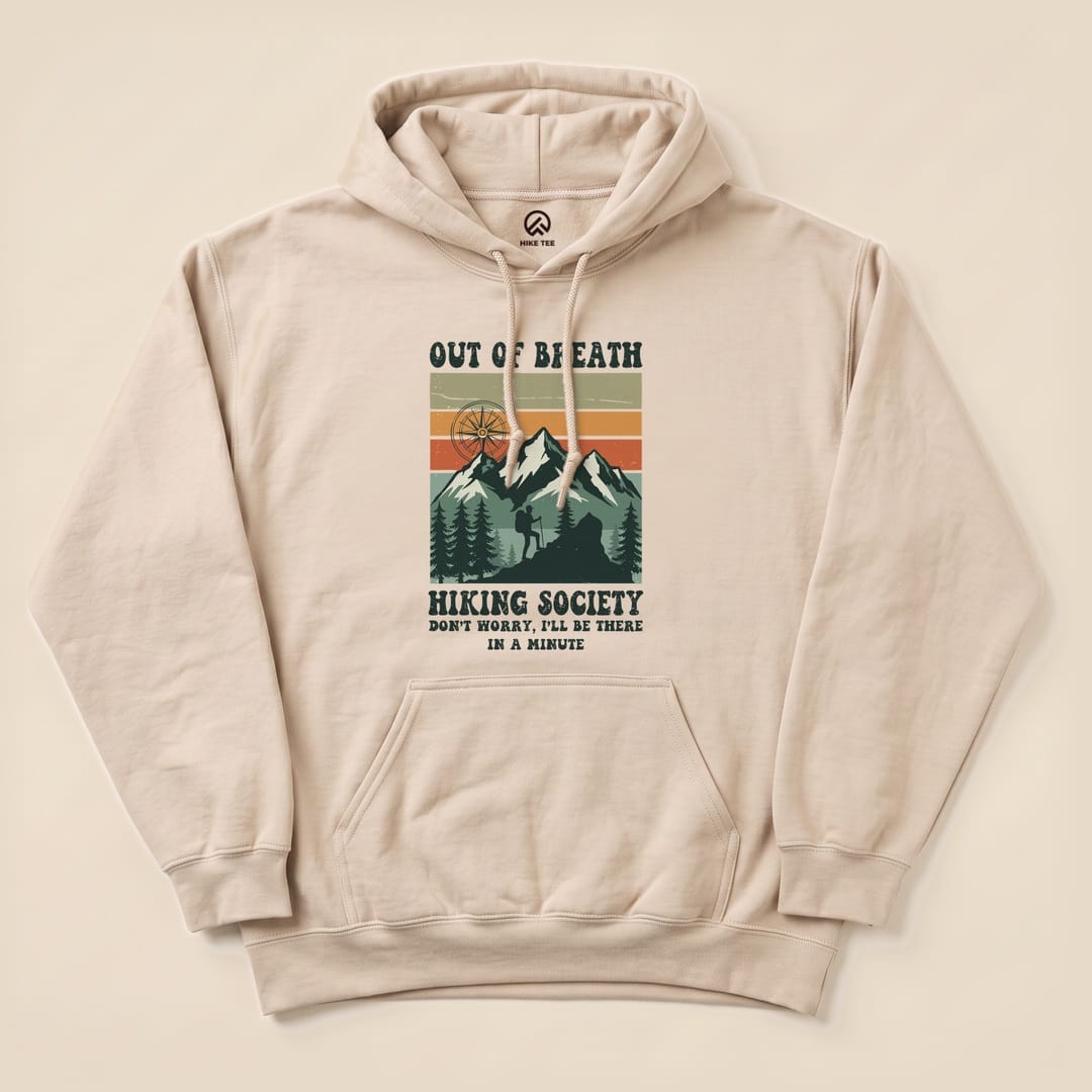 A light beige "Out of Breath Hiking Society Hoodie" features a graphic of mountains and trees with the slogan 'Don't worry, I'll be there in a minute.