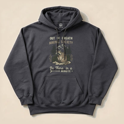 A dark hoodie featuring the "Out of Breath Hiking Society Raccoon Hoodie" graphic with a raccoon and mountains, along with the text "Be There in a Minute.