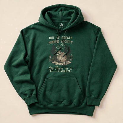 A green hoodie displaying the graphic "Out of Breath Hiking Society" above a raccoon, with the slogan "Be There in a Minute.