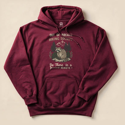 A maroon hoodie features a graphic of a raccoon with the text "Out of Breath Hiking Society" and "Be There in a Minute.