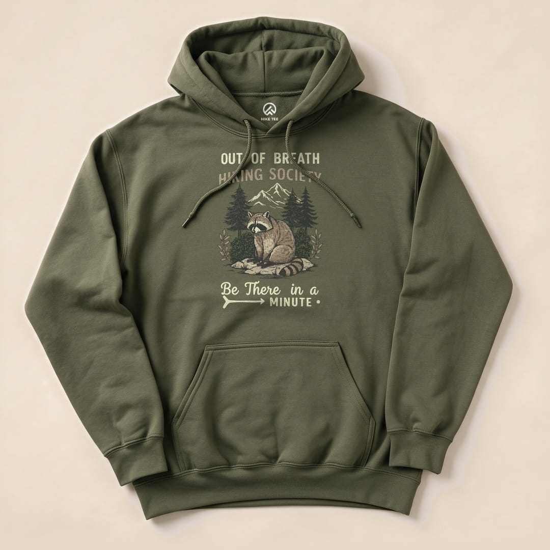 Olive green hoodie featuring a raccoon graphic with the text "Out of Breath Hiking Society" and "Be There in a Minute.