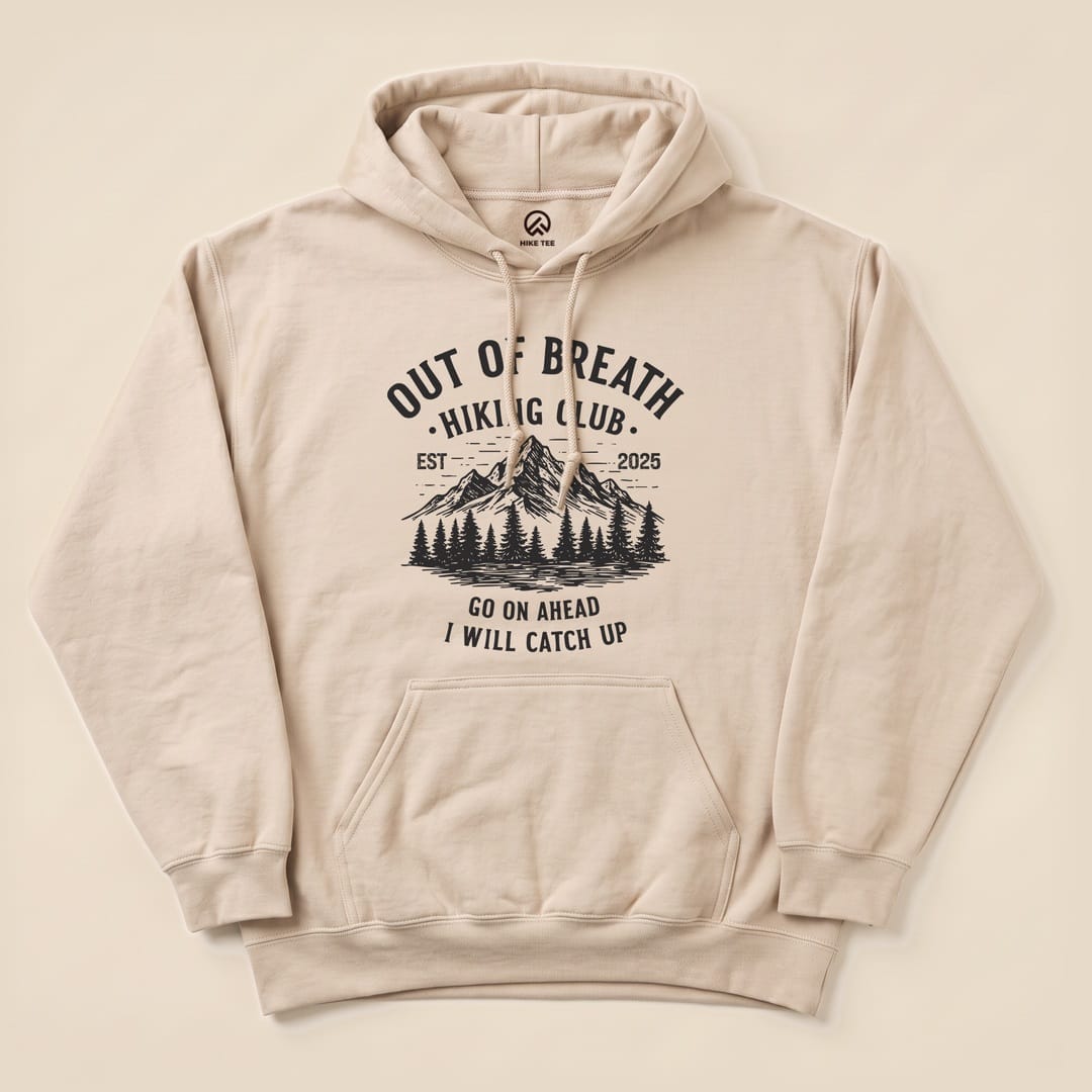 Beige hoodie featuring the "Out of Breath Mountains Hoodie" graphic design with trees and mountains, alongside the slogan "GO ON AHEAD I WILL CATCH UP.