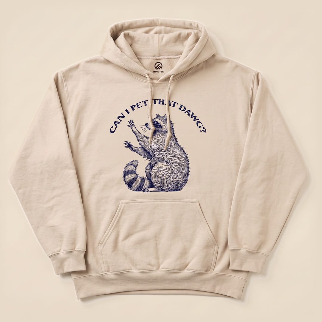A beige hoodie featuring a graphic of a raccoon with the text "CAN I PET THAT DAWG?" printed above, showcasing the Pet That Dawg Raccoon Hoodie design.
