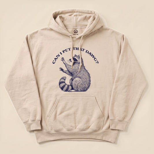 A beige hoodie featuring a graphic of a raccoon with the text "CAN I PET THAT DAWG?" printed above, showcasing the Pet That Dawg Raccoon Hoodie design.