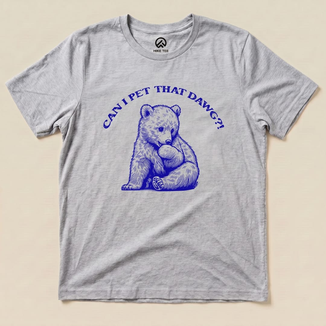 A flat graphic t-shirt in light gray featuring a blue illustration of a bear with the text "CAN I PET THAT DAWG?!".