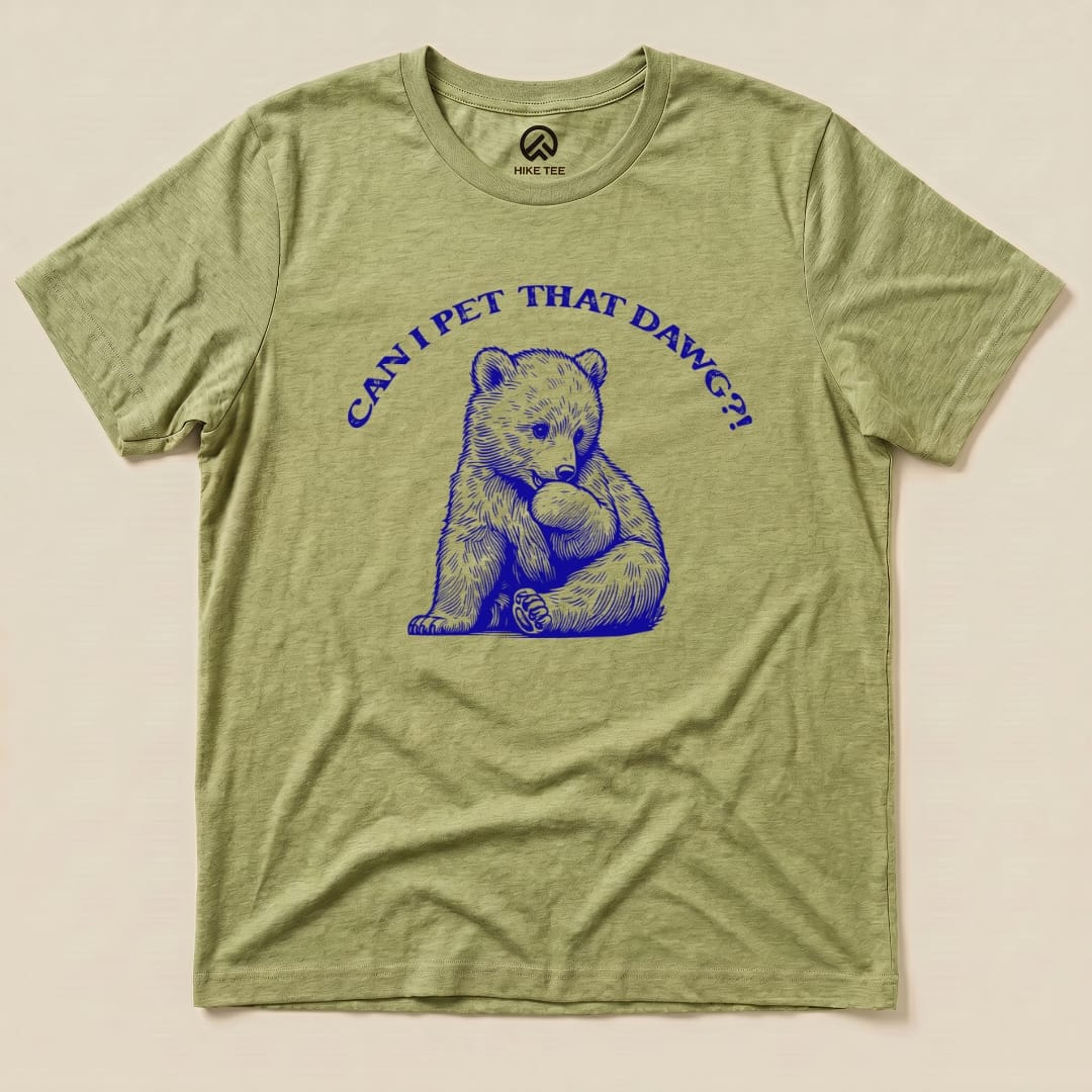 The "Pet That Dawg Shirt" features a graphic of a playful bear cub holding a rock, with the words "CAN I PET THAT DAWG?!" above it, on a light green t-shirt.