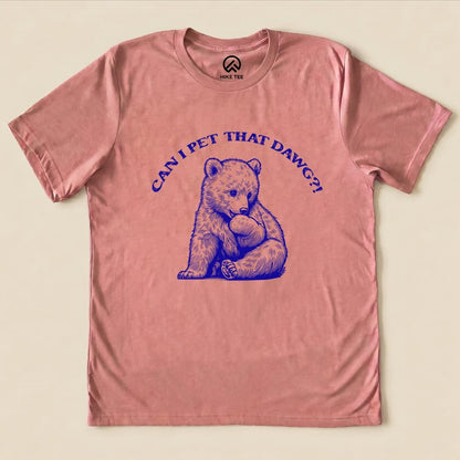 A pink graphic t-shirt featuring a cute bear illustration and the text "CAN I PET THAT DAWG?!".